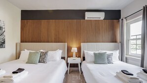 Ein Hotelzimmer mit zwei Betten, einem Nachttisch mit Lampe und einer Klimaanlage über den Betten.