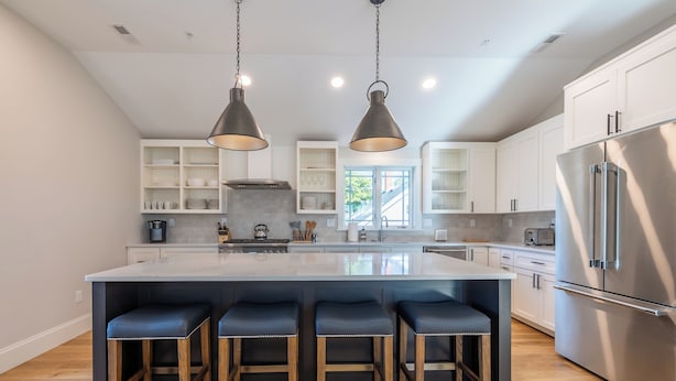 A modern kitchen with a large island, bar stools, stainless steel appliances, and pendant lighting.