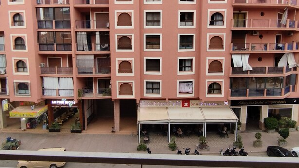 A multi-story building with balconies, a café, and a parking area. - Quiet apartment close to all amenities. (Marrakech)