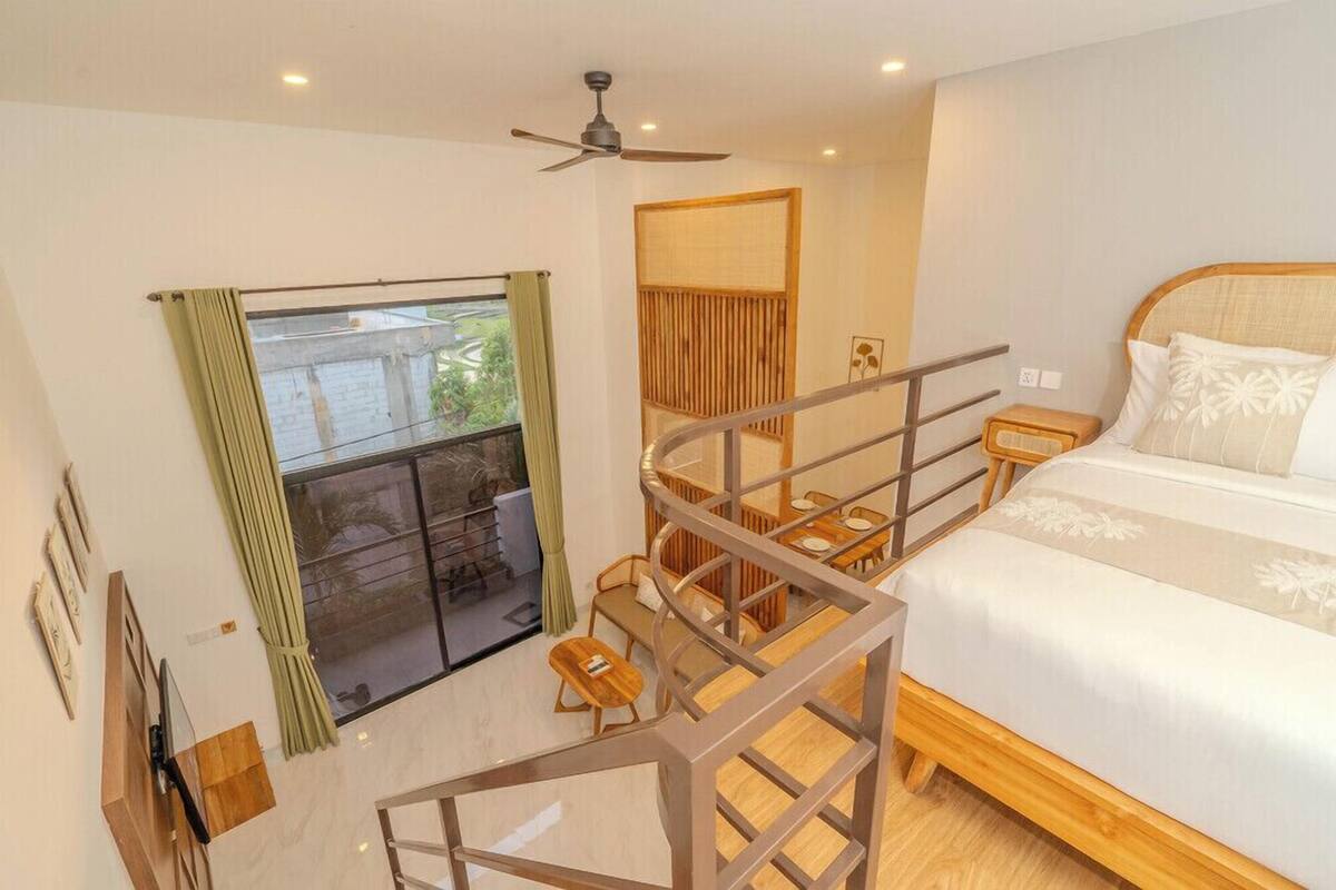 Une chambre à coucher avec un lit, une fenêtre avec des rideaux, un ventilateur de plafond et un escalier en bois.