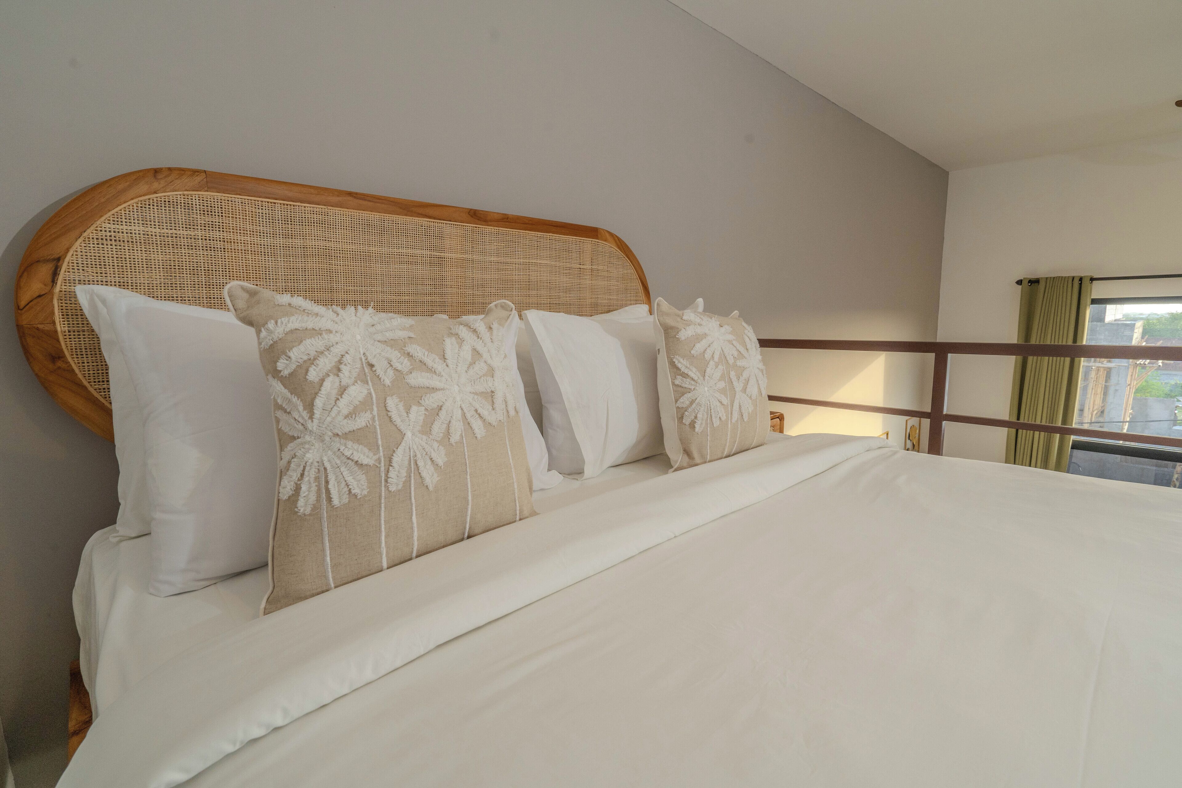 A bed with white bedding and decorative pillows, a wooden headboard, and a view of a balcony with a curtain.