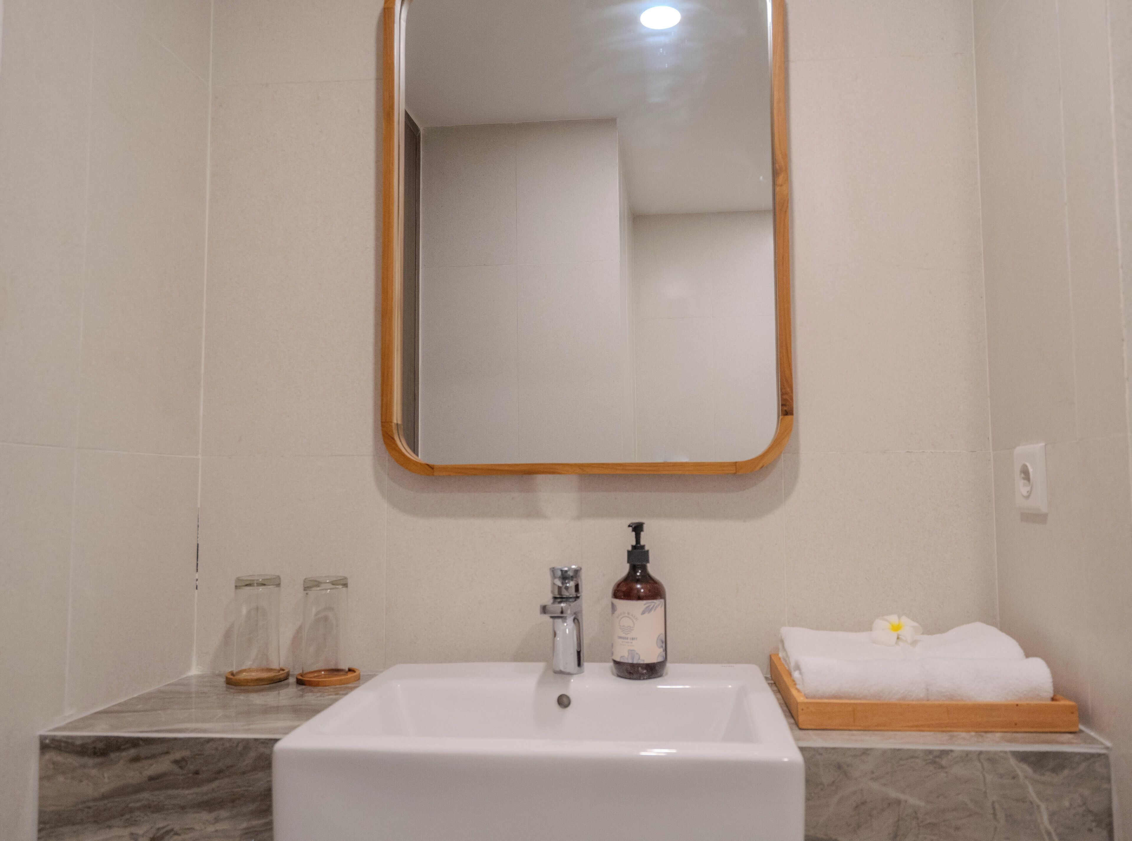 A bathroom with a white sink, a mirror with a wooden frame, a bottle of soap, and a towel on a wooden tray.
