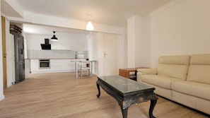 Un vaste espace de vie avec un canapé beige, une table basse en bois et une cuisine en arrière-plan.
