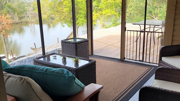 A room with a large window overlooking a lake, a wooden bench, and a wicker chair. - Dock, Deck and Game Room (Perrysburg)