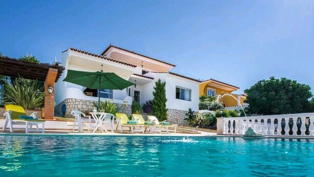 A poolside area with a house, lounge chairs, and an umbrella.