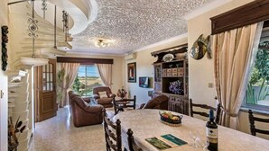 A spacious living room with a high ceiling, a dining area with a table set for two, and a view of the outdoors.