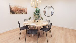 Een eetruimte met een ronde tafel, zwarte stoelen, een kroonluchter, een potplant en een ingelijst schilderij aan de muur.