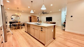 Een moderne keuken met een centraal eiland, houten kastjes en een eethoek met een ronde tafel en stoelen.