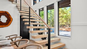 A modern staircase with wooden steps and a black railing, leading to a room with large windows and a view of trees.