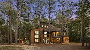 Une cabane en bois à deux étages, dotée de grandes fenêtres et d’un espace extérieur bien visible.
