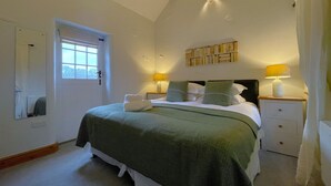 A bedroom with a bed, two bedside tables with lamps, a window, a mirror, and a bookshelf. - Deer Close Cottage - sleeps 2 guests  in 1 bedroom (Central Keswick)