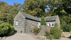 A stone house with a gravel driveway, surrounded by trees and greenery. - Deer Close Cottage - sleeps 2 guests  in 1 bedroom (Central Keswick)