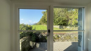 A room with a large window offering a view of a stone wall, greenery, and a distant landscape. - Deer Close Cottage - sleeps 2 guests  in 1 bedroom (Central Keswick)