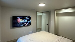 Une chambre à coucher avec un lit, un téléviseur fixé au mur, une porte et un luminaire au plafond.