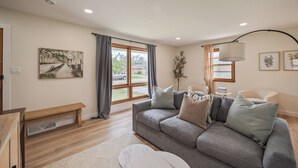 Un salon moderne avec un canapé gris, un banc et une grande fenêtre agrémentée de rideaux.