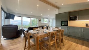 A modern kitchen with wooden cabinets, a built-in microwave, and a dining area with a wooden table and chairs. - Swallows Lodge - Modern accommodation with breathtaking views (Keswick)