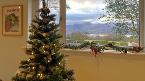 A Christmas tree with lights and decorations near a window with a view of mountains and trees. - Swallows Lodge - Modern accommodation with breathtaking views (Keswick)