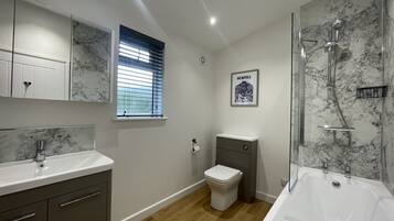 Een moderne badkamer met een marmeren spatwand, een vrijstaand bad, toilet en een wastafel met spiegel.