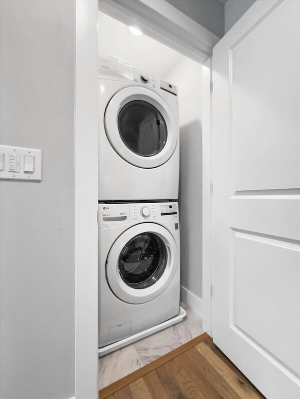 A laundry room with two stacked front-loading washing machines, a wooden floor, and a white door.