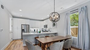 Une cuisine moderne avec des meubles blancs, un réfrigérateur en acier inoxydable et une table à manger en bois, accompagnée de chaises.