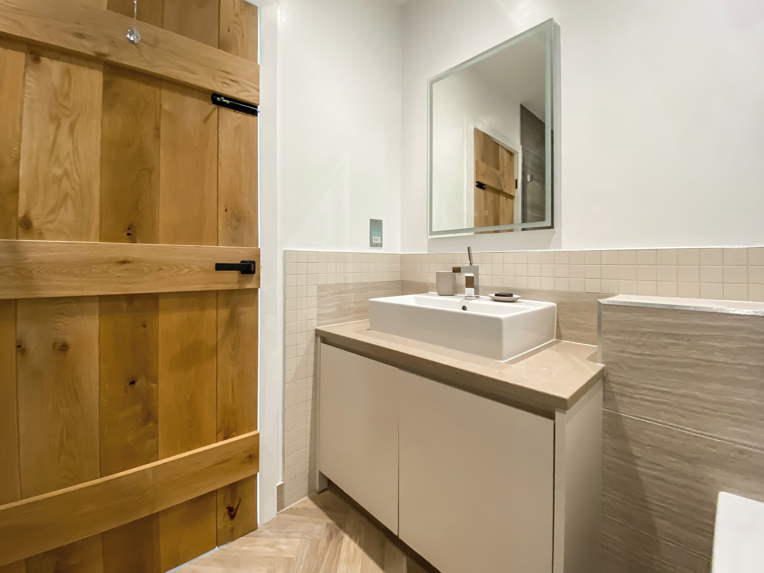 A modern bathroom with a wooden door, a white sink, and a mirror above it.