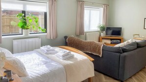 Une chambre bien rangée, avec un lit, un canapé, une télévision et une plante en pot.