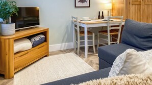 Un salon confortable avec un canapé, un téléviseur posé sur un meuble en bois, une table à manger avec des chaises et une lampe.