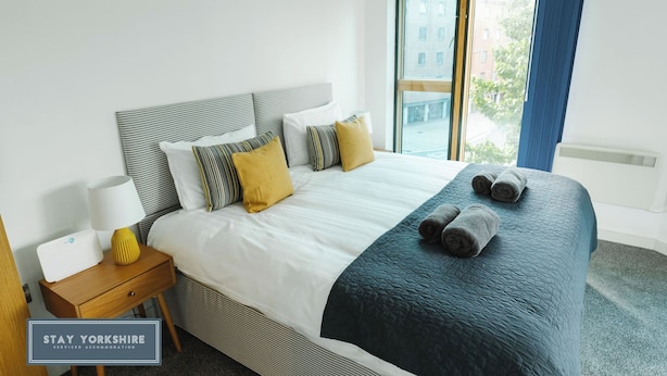 Ein Hotelzimmer mit Bett, Nachttisch, Lampe und Blick ins Freie.