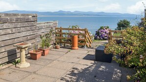 Eine Terrasse mit Kübelpflanzen, einem Holzzaun und Blick auf das Meer.