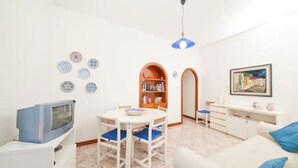 A small, bright living room with a television, a dining table, and a bookshelf. - Cozy apartment with breathtaking views in Positano. CIN IT065100C2D8D7L43H (Positano)