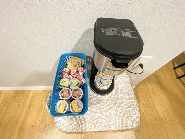 Une machine à café posée sur un support, avec un panier bleu contenant différentes capsules de café.