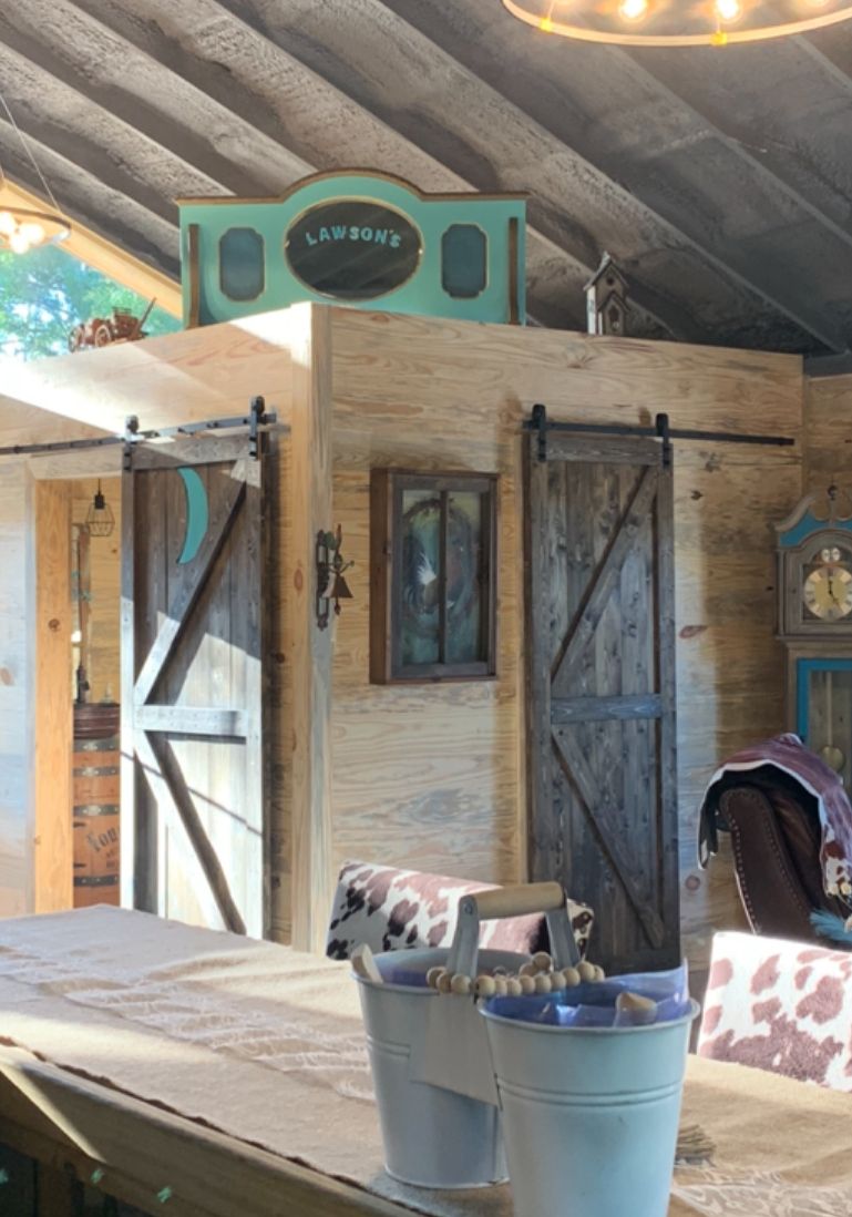 Un intérieur rustique avec une porte en bois portant l’inscription « LAWSON », une petite fenêtre et une table avec des seaux.