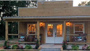 A rustic wooden building with a porch, a sign reading "FRIENDS", and outdoor seating with cowboy hats. - Charming farmhouse in delightful Brantley with AC (Brantley)