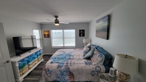 A bedroom with a bed, a TV, a dresser, and a window with blinds.