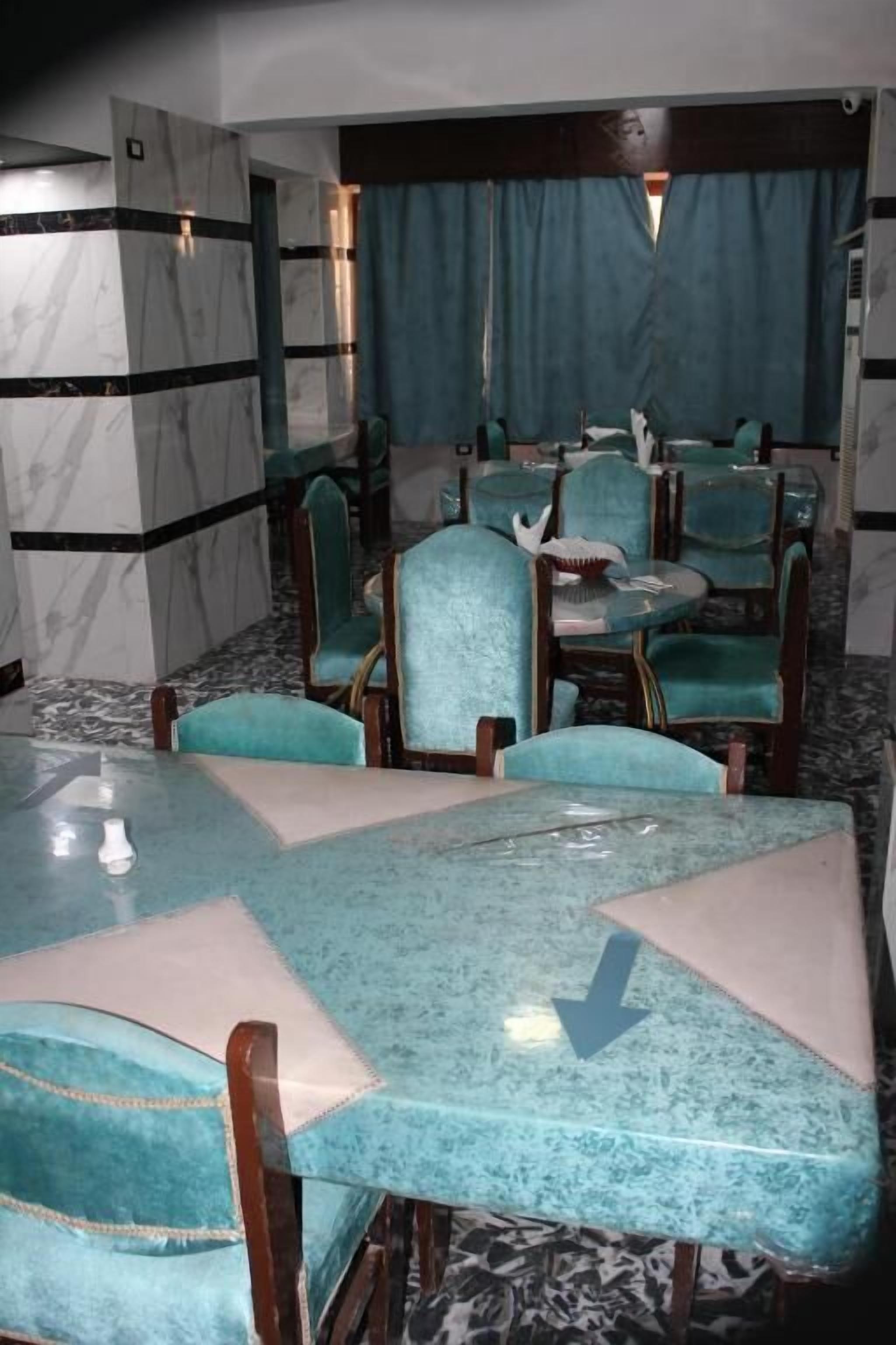 A dining area with a marble wall, teal upholstered chairs, and a glass table.