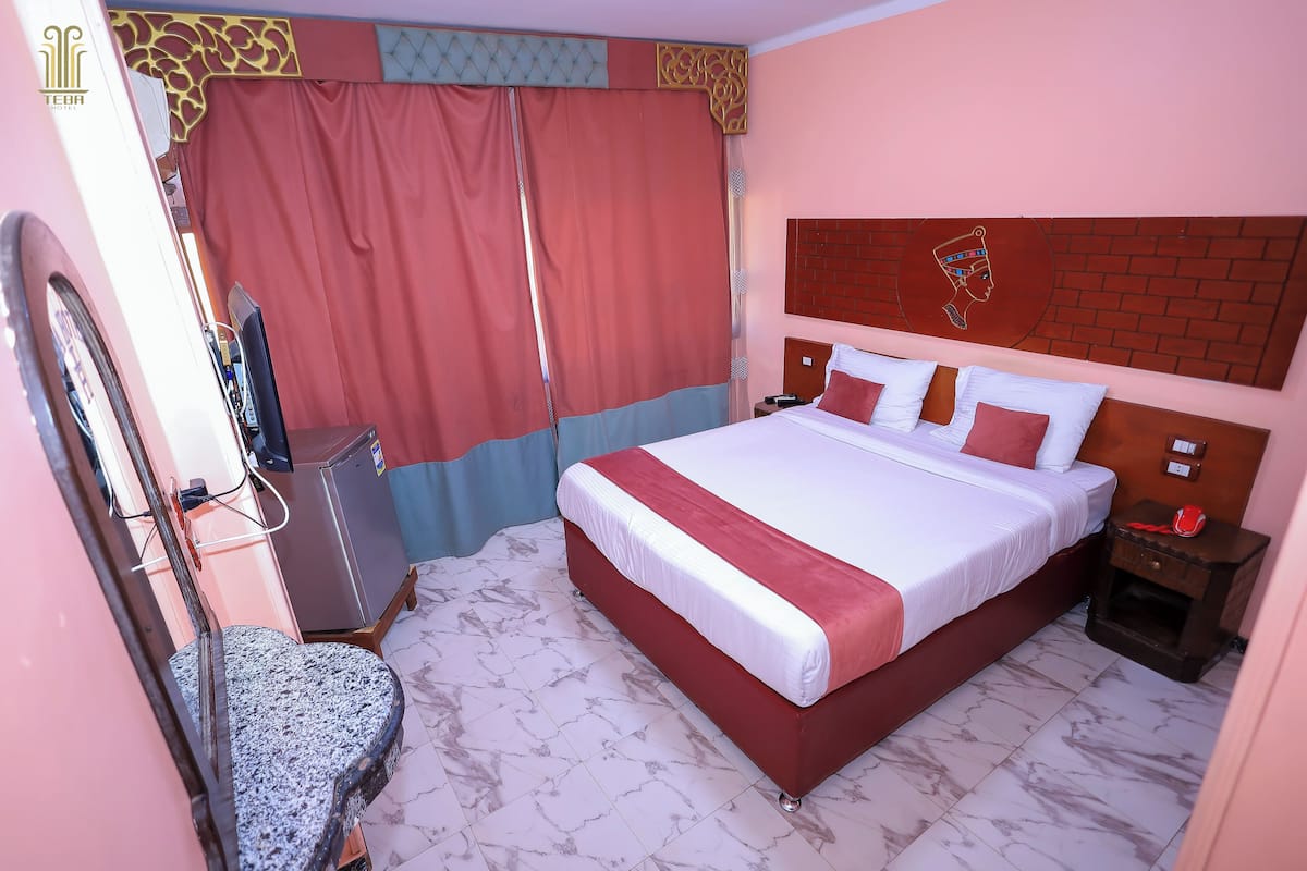 A hotel room with a large bed, a TV, a desk, and a mirror.