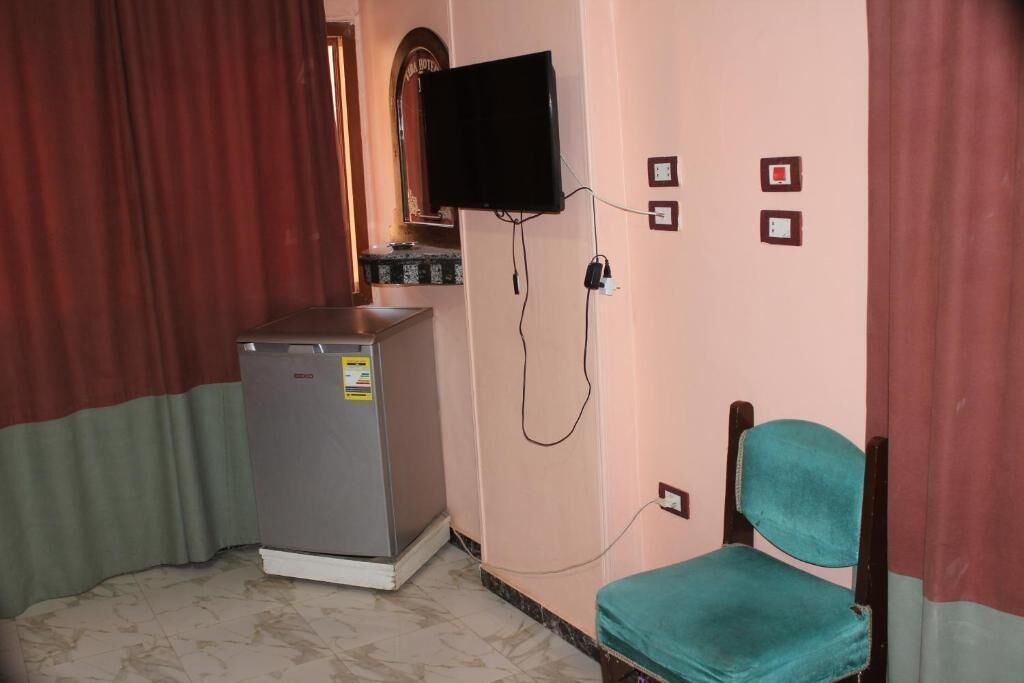 A small room with a refrigerator, a television mounted on the wall, and a single chair.