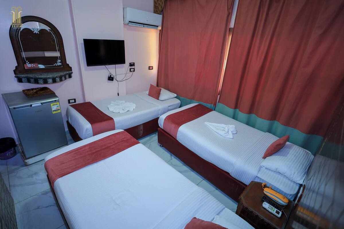 A hotel room with three beds, a television, an air conditioner, and a small desk with a computer and a telephone.