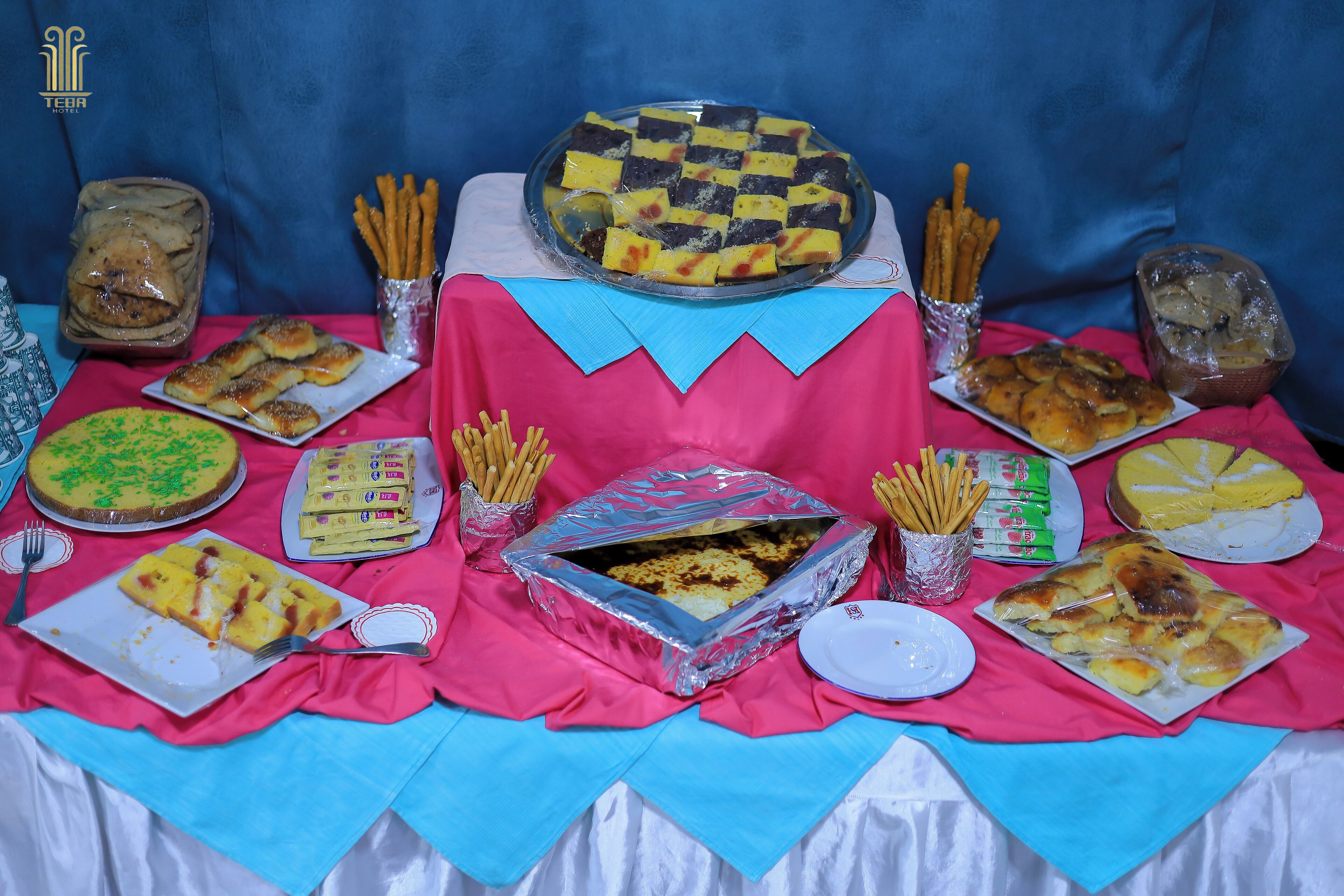A table with various food items, including a large checkered cake, pastries, and a tray of breadsticks.