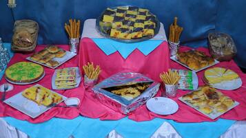 A table with various food items, including a large checkered cake, pastries, and a tray of breadsticks.