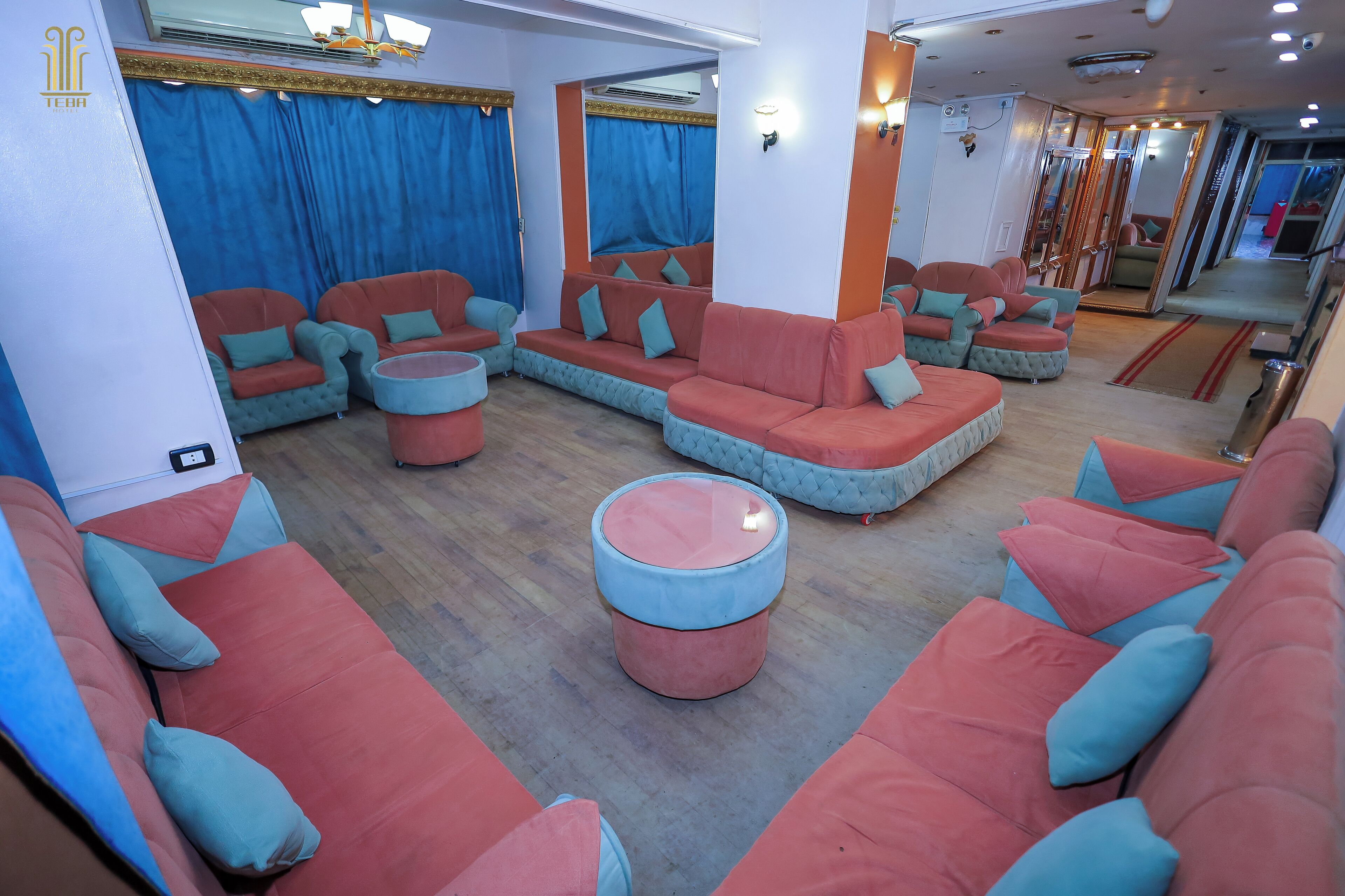 A modern lounge area with multiple seating options including sofas and ottomans, a large mirror, and a visible door leading to another room.
