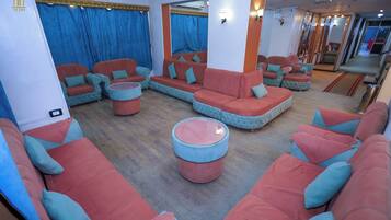 A modern lounge area with multiple seating options including sofas and ottomans, a large mirror, and a visible door leading to another room.