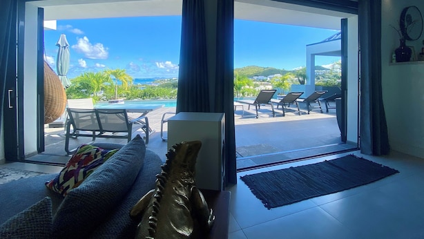 Un soggiorno moderno con un divano, una scultura decorativa a forma di pesce e vista su una piscina e un'area relax all'aperto.