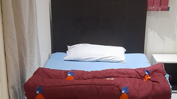 Un lit avec une tête de lit noire, un matelas bleu et une couverture rouge ornée de motifs orange et bleu.