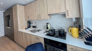 Eine moderne Küche mit Holzschränken, einer Edelstahl-Spüle, einem Gasherd und einem gelben Wasserkocher.