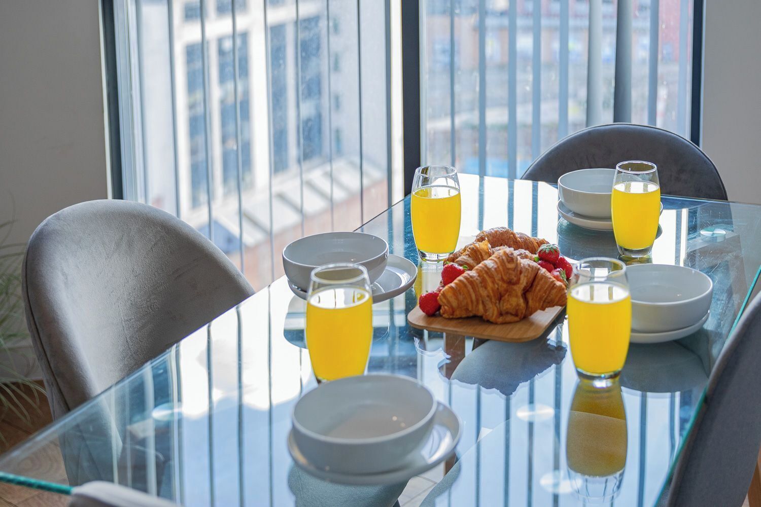 Une table de petit-déjeuner avec des croissants, du jus d’orange et des tasses de café.