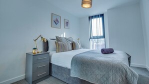 Un dormitorio con cama, mesita de noche, lámpara y una obra de arte en la pared.