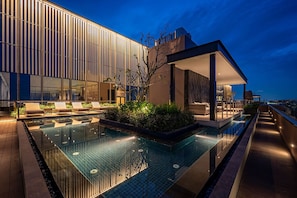 Un hotel moderno con piscina a sfioro sul tetto, area relax e vista sullo skyline cittadino al crepuscolo.