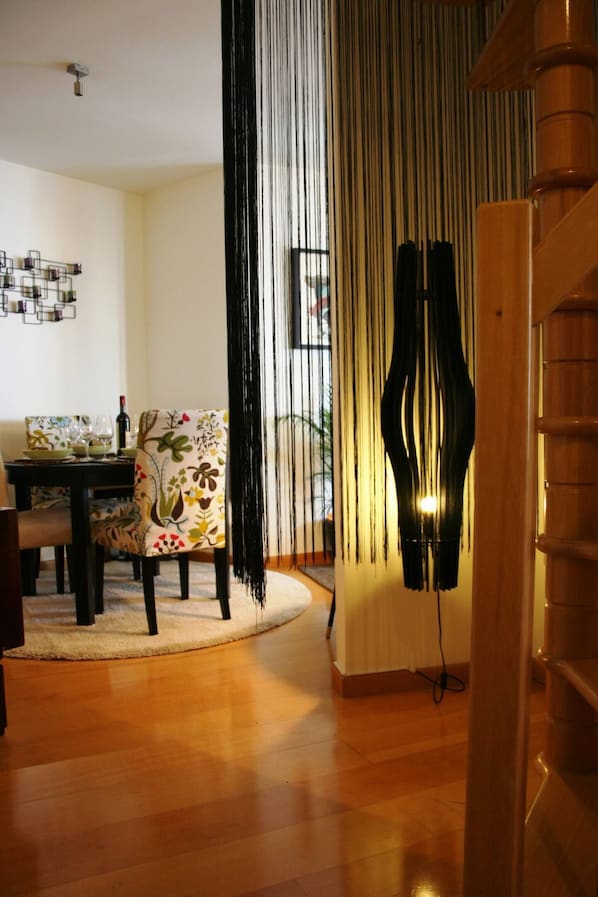 A dining area with a table set for two, a chair with a floral pattern, and a black abstract sculpture.