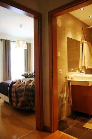 A hotel room with a bed, a bathroom with a sink and mirror, and a wooden door frame.